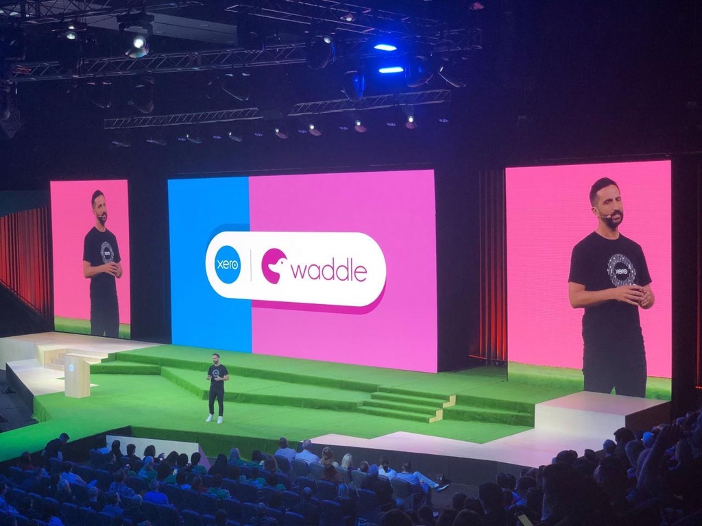 Leigh Dunsford on stage at Xero, with the Waddle logo on the screen behind him